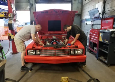 Team working under the hood of Orange Ford Fairmont