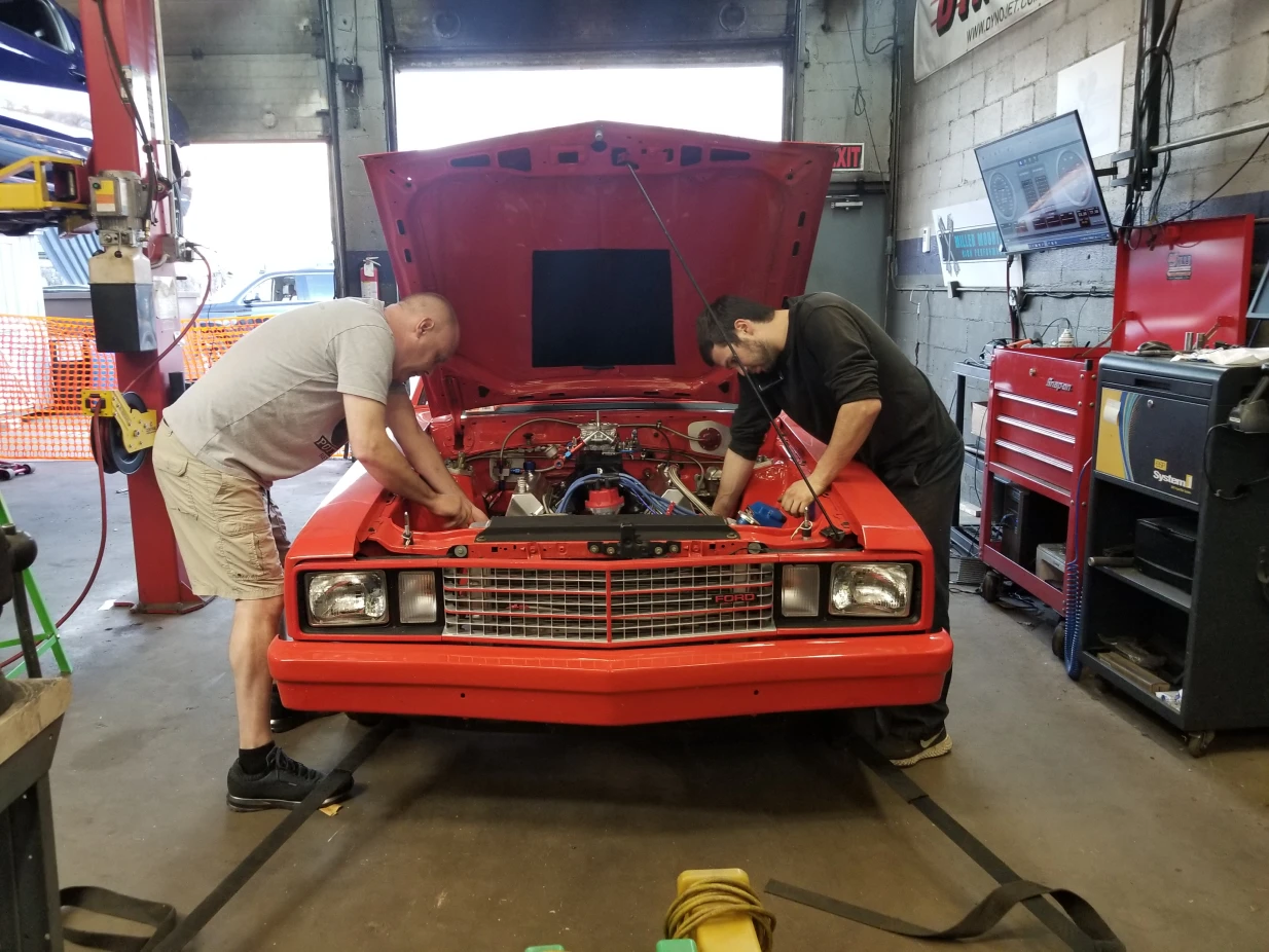 Team working under the hood of Orange Ford Fairmont
